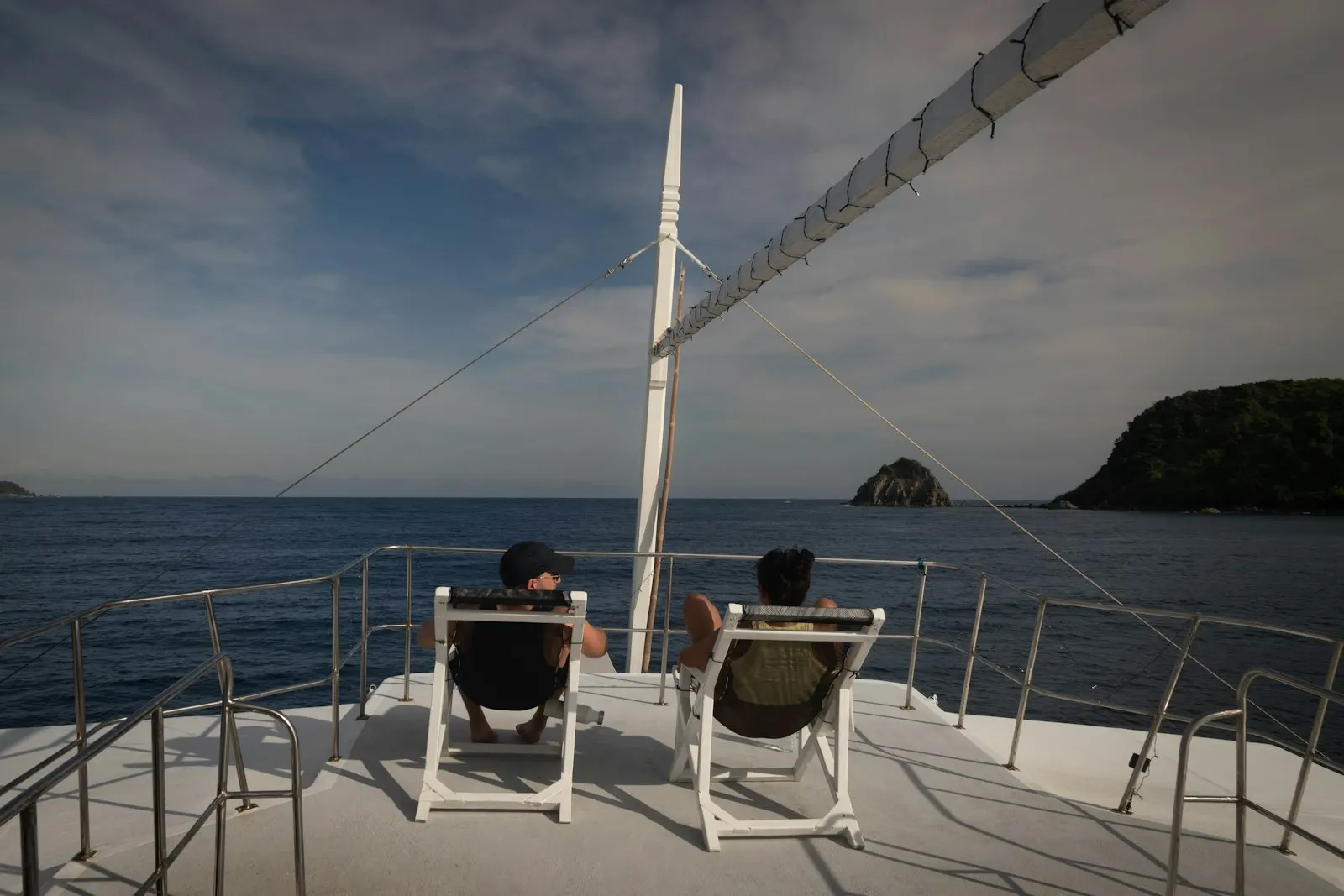 Two people relax on a boat deck overlooking the ocean.