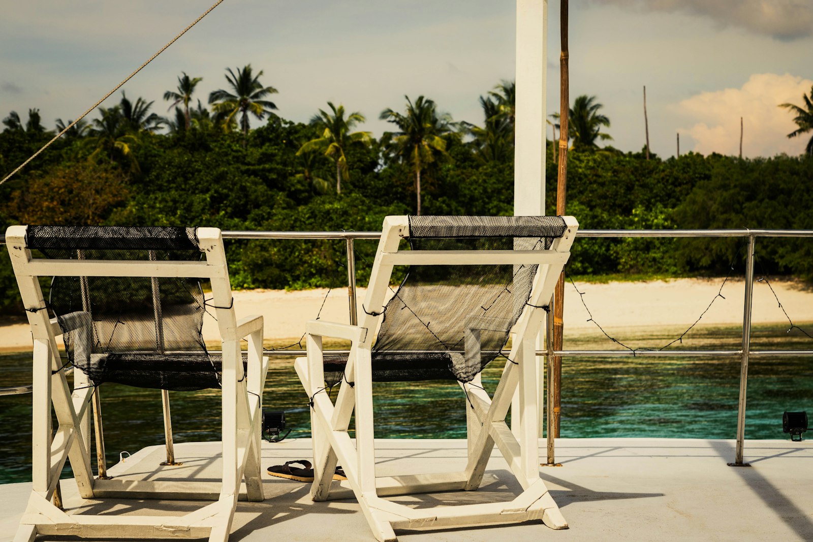 Two chairs on a deck overlooking a tropical beach.